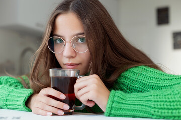 Young girl with glasses holding a glass of tea. Young girl with long brown hair wearing glasses and...