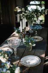 Beautiful summer dinner table setting outdoors, with vintage plates, candles, wine glasses and jasmine and forget me not flowers on the wooden table 
