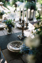 Beautiful summer dinner table setting outdoors, with vintage plates, candles, wine glasses and jasmine and forget me not flowers on the wooden table 