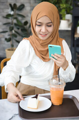 Young Muslim woman content creator taking photo and video content while arranging delicious halal iced milk tea and blueberry cheesy cake, concept image for SNS, Blog, Vlog content creation