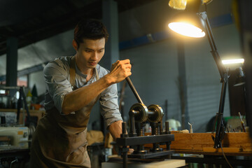 Young leather craftsman using a manual rolling machine working on a leather project in workshop