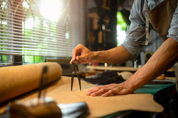 Close up of an artisan hands meticulously measuring a piece of leather using a pair of dividers in workshop