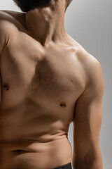 Close up photo of athletic man shirtless, in black pants, displaying his toned physique in elegant pose against grey background. Concept of man's fashion and style, beauty and youth, masculinity.