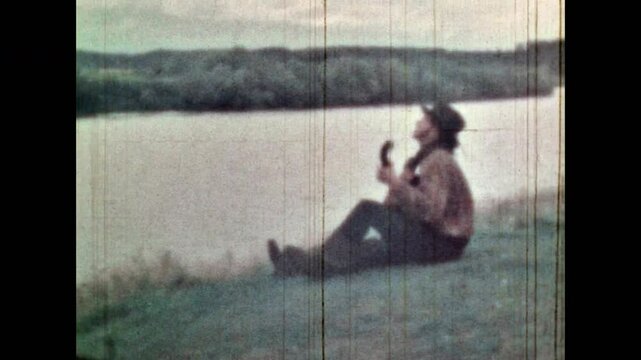 Man playing guitar on scenic summer nature background. Romantic musician play in music instrument, enjoy river, green meadow natural landscape. Vintage color film. Art archive outdoors. Retro 1960s