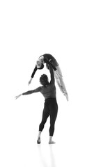 Fluidity and strength. Man and woman, ballet pair practice together against white studio background. Black and white filter. Concept of pair training, classic ballet, inspiration, beauty, creativity.