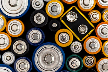 Background made of various alkaline and lithium-ion batteries, positive pole visible.