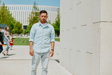 Young man walking outdoors in a modern urban setting on a sunny day, looking pensive and deep in...