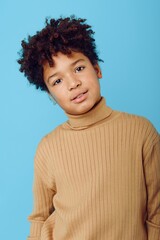 Young african american boy in tan turtleneck sweater posing confidently against a striking blue background