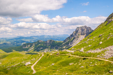 Naklejka premium A dirt road winds through a lush mountain valley under a clear sky
