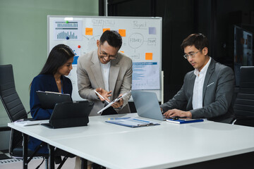 Asian businessman showing hand and smiling young team of colleagues making good business discussion in modern coworking office concept teamwork people.