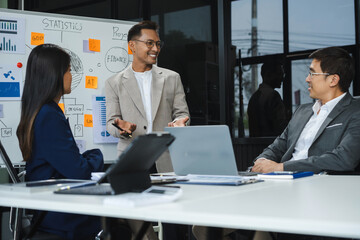 Asian businessman showing hand and smiling young team of colleagues making good business discussion in modern coworking office concept teamwork people.