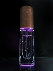 Women's perfume in neon purple backlight. Perfume water. Perfume on a black background. Place for text, background. A bottle of perfume in close-up.