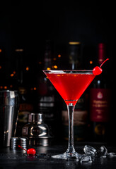Red alcoholic cocktail drink with cherry on dark background, bar counter with bottles