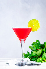 Red alcoholic cocktail drink with vodka, liqueur, cranberry, juice, lime and ice. in martini glass Gray background