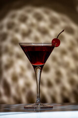 Black Manhattan alcoholic cocktail with whiskey and red vermouth garnished with maraschino cherry in martini glass. Beige background, hard light