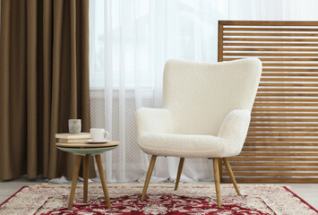 Soft armchair, coffee table and window with curtains in room. Interior design