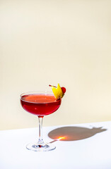 New Yorker red cocktail with whiskey, grenadine, bitter, lemon and ice garnished with lemon zest and cocktail cherry in glass. Beige background, hard light