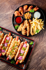 Assorted fast food items including hot dogs, chicken wings, fries, and fried chicken tenders served on black plates.