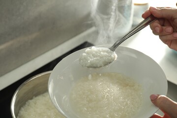 Woman putting boiled rice into bowl, closeup