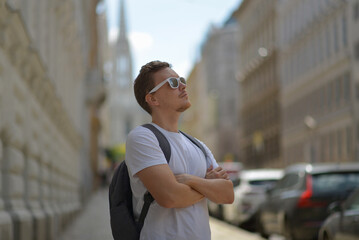 A man wearing white sunglasses and gray backpack on the street in Vienna on a hot sunny summer day. Tourism and sightseeing concept