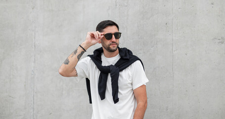 cool fashion successful guy with a beard and hairstyle in fashionable casual clothes puts on...