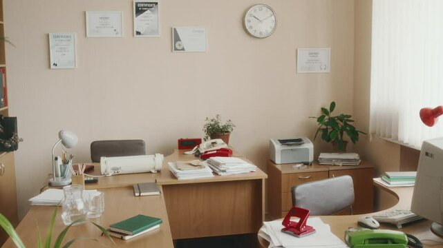 No people pan shot of empty retro vintage office in light colors with wooden desks and old devices. Computer, printer, typewriter and stacks of papers on tables, certificates on wall