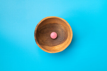 Minimalist concept of medicine, health care, pharmaceuticals. Pink tablet, vitamin in a wooden bowl on blue background, flat lay top view copy space 