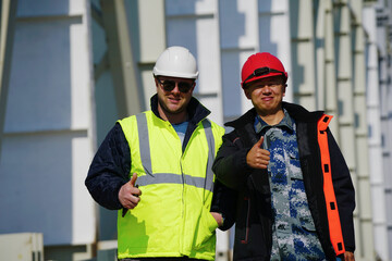 Two multiracial construction workers or engineers walking side by side through a construction site, conversing.                        