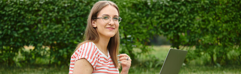 A young woman smiles while using her laptop outdoors.