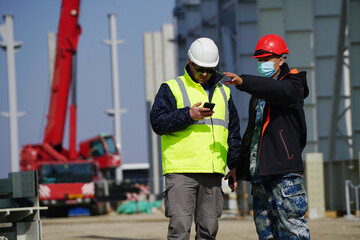 Two multiracial construction workers or engineers walking side by side through a construction site, conversing.                        