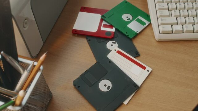 No people top view of vintage black, green and red diskettes lying on wooden office desk near keyboard and printer, 90s