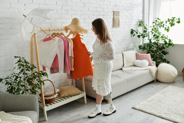 A young woman with a prosthetic leg stands in front of a clothing rack, selecting an orange dress...