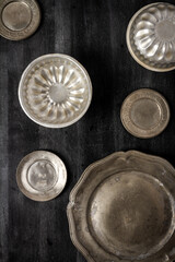 Vintage pewter plates and bowls on black chalkboard background. Flat lay. Top view. Food concept. Dark mood food photography.