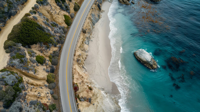 Aerial view of a scenic coastal highway running alongside a sandy beach and turquoise ocean, bordered by rugged cliffs and vegetation