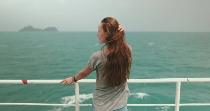 A woman stands railing ferry boat, looking tropical ocean. The sea is a vibrant turquoise, with gentle waves rippling across its surface. Girl enjoy fresh air and stunning views of tropical paradise.
