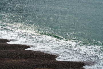 Symmetric clear sea waves on the pebble beach of Etretat during the low tide. 