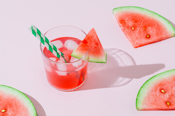 Summer scene with tropical refreshing watermelon drink and slices of fresh watermelon on pink background. Sun and shadows. Minimal cocktail concept. Trendy summertime party idea. Summer aesthetic.