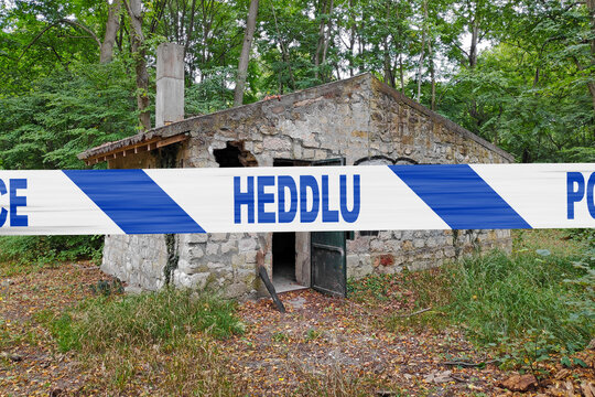 Welsh police tape in front of an abandoned stone house in the woods