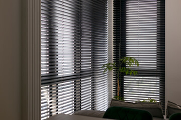 Wooden automatic blinds partially open, covering large corner windows in the interior. Sunlight...