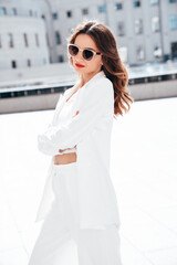 Fototapeta premium Young beautiful brunette woman wearing nice trendy white suit jacket. Sexy smiling model posing in the street at sunny day. Fashionable female outdoors. Cheerful and happy. Sunglasses. crossed arms