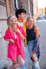 Group of young three stylish friends posing in the street. Fashion man and two cute female dressed in casual summer clothes. Smiling models having fun. Cheerful women and guy outdoors
