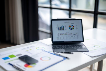 A laptop is on a table with a bunch of papers and a cell phone