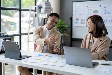 Two people are sitting at a desk with a white board behind them