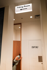 An adult woman peeking into a fitting room of a clothing store in a mall