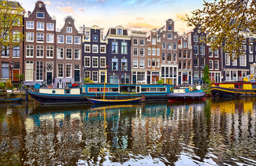 Fototapeta premium Amsterdam, Netherlands. Panorama of famous dancing houses on river Amstel, water channels with house boats. Popular landmark and travel destination in old european city. Evening sunset landscape