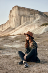 Serene woman in hat sitting in front of majestic mountain landscape