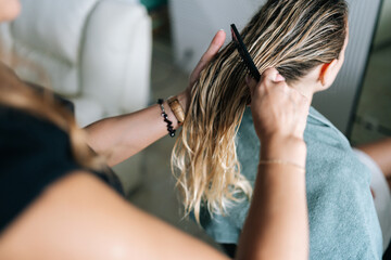Fototapeta premium Close-up of unrecognizable hairstylist brushing wet long hair with hairbrush after washing. Closeup of blonde female client getting hair dressed in beauty salon. Concept of fashion hairstyling.