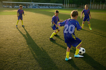 Young soccer players, boys in blue uniforms practicing passing ball skills, training soccer game on sunny field, demonstrating enthusiasm. Concept of sport, childhood, education, active lifestyle