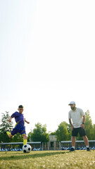Obraz premium Young athlete striking soccer ball with determination, while coach controlling and navigating movements. Outdoor soccer training. Concept of sport, childhood, education, achievement, active lifestyle