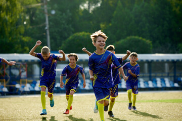Obraz premium Happy and excited boys, children in sportswear running on field, expressing happiness and success after winning match. Team spirit. Sport, childhood, education, achievement, active lifestyle concept